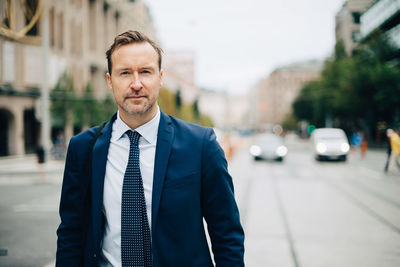 Portrait of confident mature businessman walking on street in city