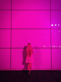 Rear view of woman standing by illuminated pink wall at night