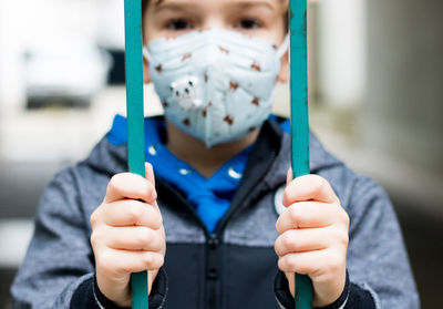 Close-up of boy with face mask standing behind gate during covid-19 lockdown.