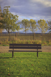 Empty bench in park against sky