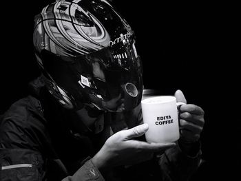 Man wearing helmet holding coffee against black background