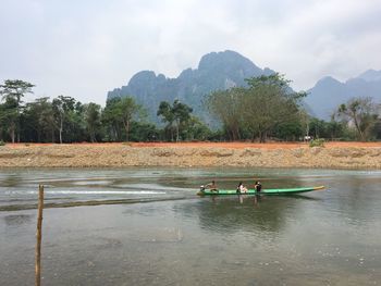 People on boat in lake against sky