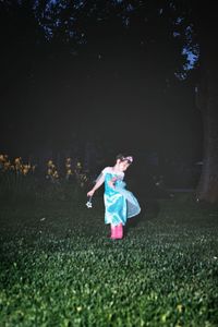 Girl wearing fairy costume standing on grassy field at night