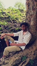 Portrait of young man sitting on tree trunk