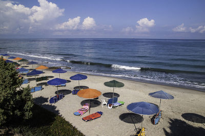 Colorful parasols and deck chairs on shore at beach against sky
