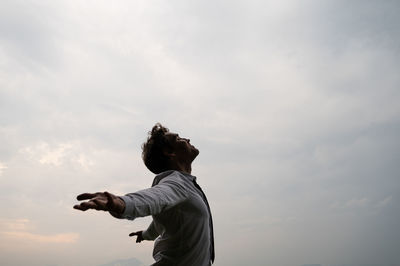 Side view of man with arms outstretched standing against sky