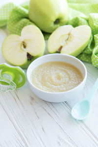 Bowl with baby food and apples on table
