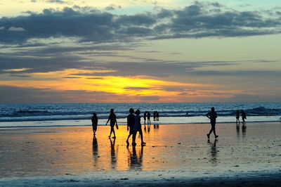 Silhouette people standing on beach against sky during sunset