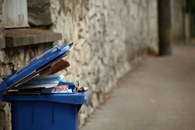 Close-up of carbage bin on footpath against wall