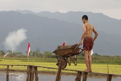 Man carrying firewood in wheelbarrow on narrow footbridge