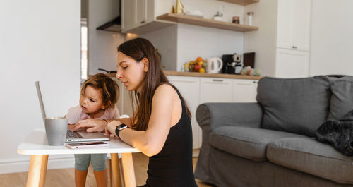 Toddler looking at shocked mother with laptop at home