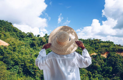 Rear view of person in hat standing against trees and sky