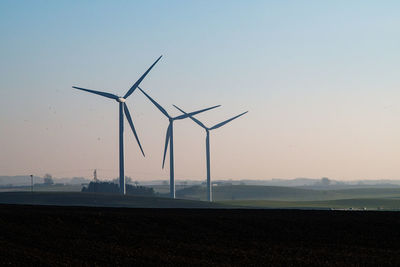 Windmills on field against clear sky during sunset