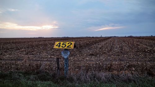 Sign board at farm against cloudy sky during sunset
