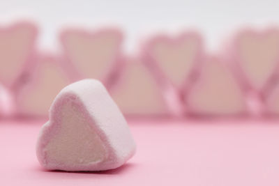 Close-up of pink heart shaped marshmallows on table against white background