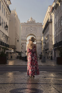 Rear view of woman standing on street amidst buildings in city