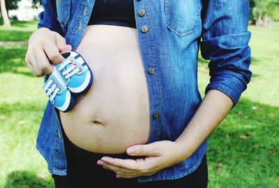 Midsection of pregnant woman holding belly and baby booties in park