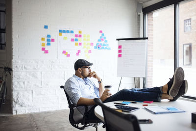 Thoughtful businessman holding disposable cup while sitting at creative office