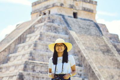 Portrait of smiling young woman wearing hat while standing against monument