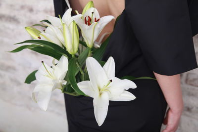 Fashion details, bouquet of white lilies is hidden in the dress of a girl, who is standing backwards