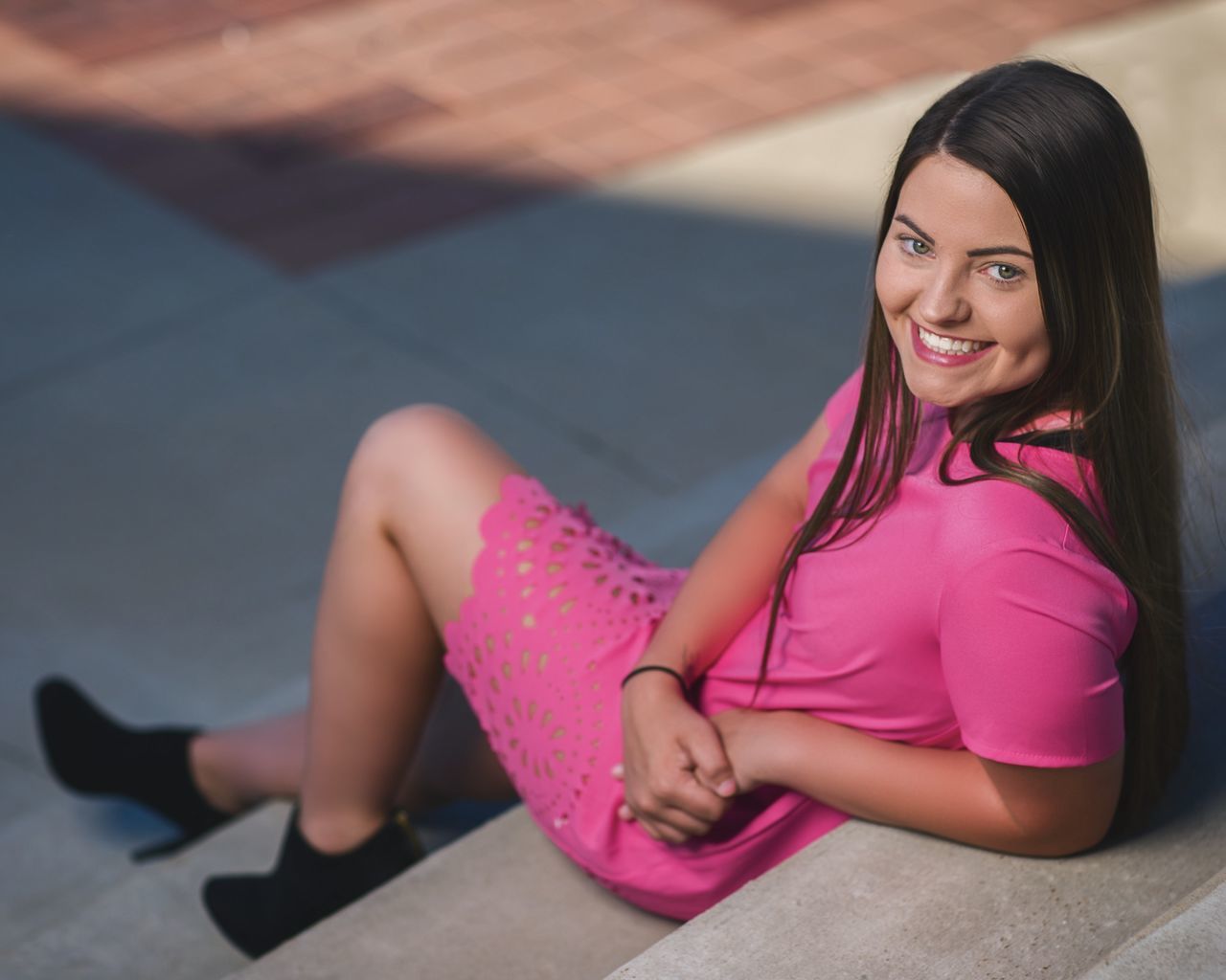 one person, looking at camera, smiling, young adult, sitting, real people, young women, lifestyles, portrait, women, leisure activity, beautiful woman, beauty, pink color, full length, happiness, focus on foreground, adult, casual clothing, hairstyle