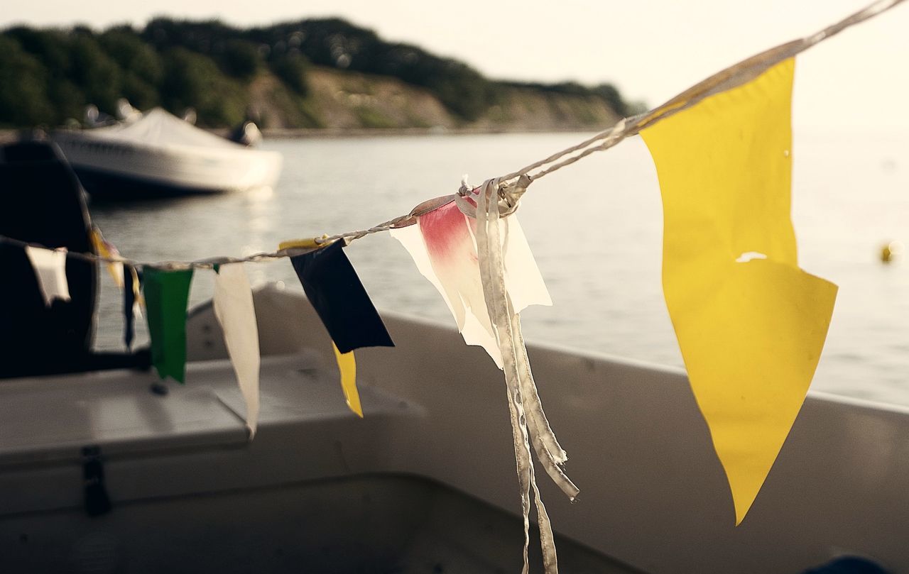focus on foreground, yellow, hanging, no people, water, day, nature, close-up, clothesline, rope, clothing, outdoors, nautical vessel, lake, flag, security, mode of transportation, clothespin