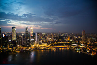 Illuminated buildings by river against sky at night