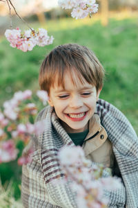 Portrait of a funny little boy wrapped in a blanket enjoying cherry blossoms in a city park.