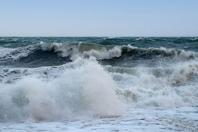 Waves splashing on shore against clear sky