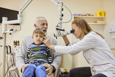 Ent physician examining ear of a boy sitting on grandfather's lap