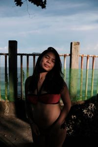 Portrait of young woman in bikini standing against sky