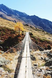 Footbridge by mountain against sky