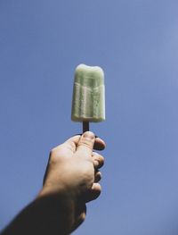 Hand holding ice cream against blue sky