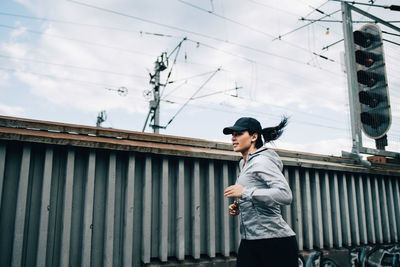 Young sportswoman jogging by fence on footbridge in city