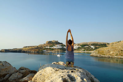 Man standing on rock by sea against clear sky