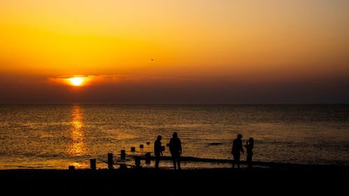 Silhouette people on beach against sky during sunset