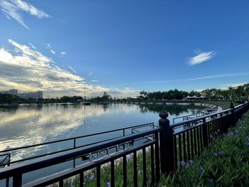 Man standing on railing by lake against sky