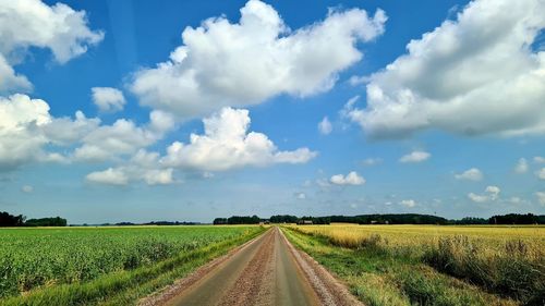 Empty road amidst field against sky