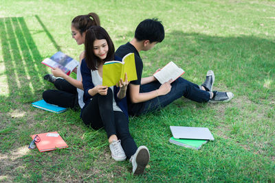 High angle view of friends studying while sitting on grassy field at park