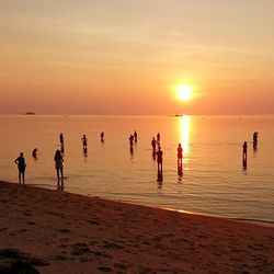Silhouette people on beach against sky during sunset