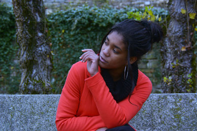 Young woman looking away while sitting against tree