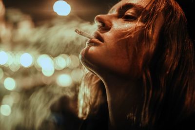 Close-up of teenage girl smoking cigarette at night