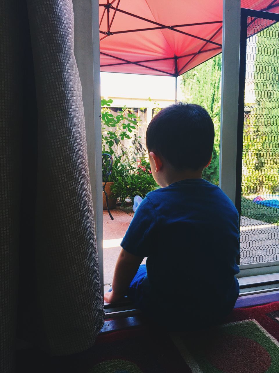 REAR VIEW OF YOUNG WOMAN LOOKING THROUGH WINDOW