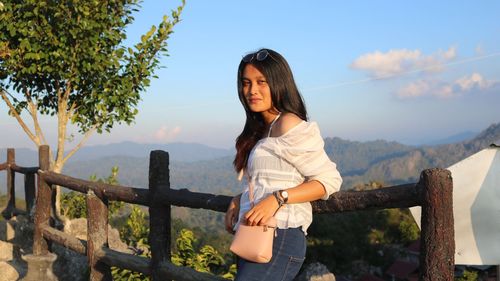 Young woman standing by railing against mountains