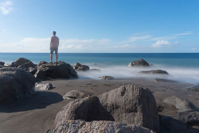 Rear view of man standing on rock at beach