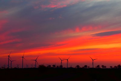 Silhouette of wind turbines on field against orange sky