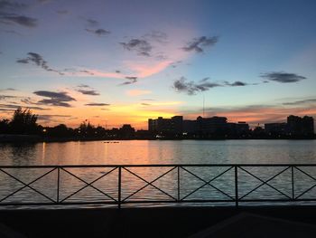 Silhouette buildings by river against sky during sunset