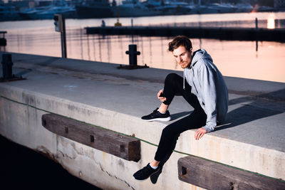 Full length of young man sitting on railing by water