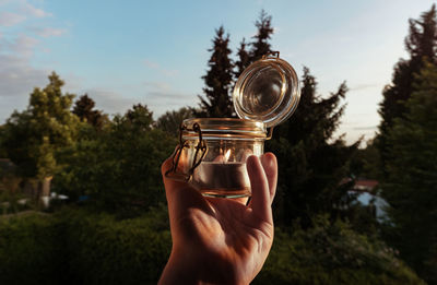 Cropped hand holding lit tea light against sky