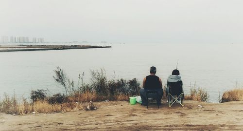 Rear view of couple sitting on beach against clear sky